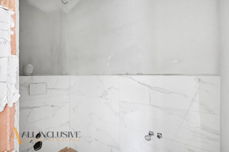 Koupelna v rodinném domě s bílými mramorovými obklady bez zařizovacích předmětů.