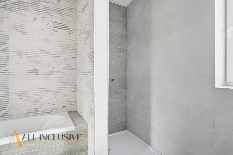 Koupelna v rodinném domě s vanou a sprchovým koutem, světlé obklady.