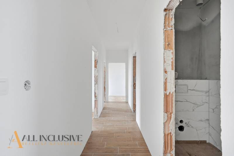 Chodba v rodinném domě s bílými stěnami a podlahou s dřevěným dekorem.