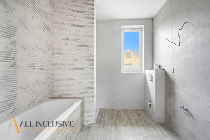 Koupelna v rodinném domě s vanou, šedými obklady a podlahou s dřevěným dekorem.