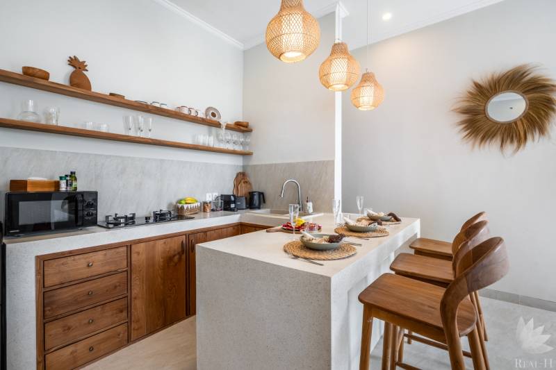 Kuchyně vily se stylovými dřevěnými prvky, barovými stoličkami a závěsnými lampami.