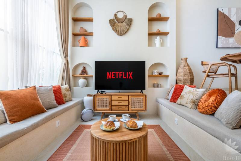 Pohodlný obývací pokoj ve vile s televizí, polštáři a dekoracemi, podává se káva.