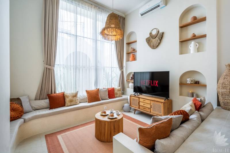 Světlý obývací prostor ve vile s pohovkou, TV a dekorativním osvětlením.