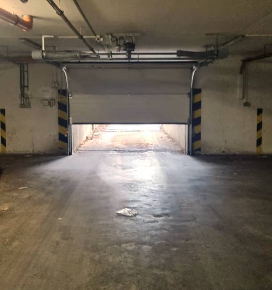 Otevřená garážová vrata vedou ven, okolí je osvětlené nepřímým světlem.