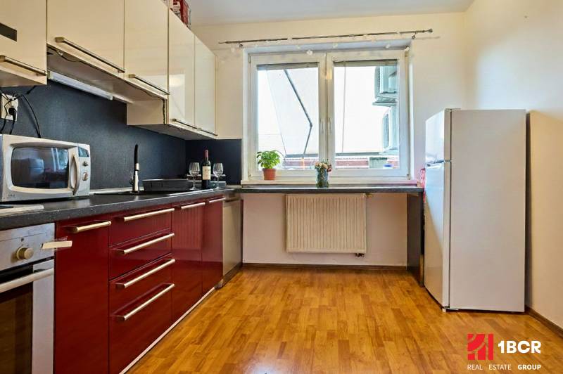 Kuchyně v 2-pokojovém bytě s červenými skříňkami a podlahou s dřevěným dekorem.