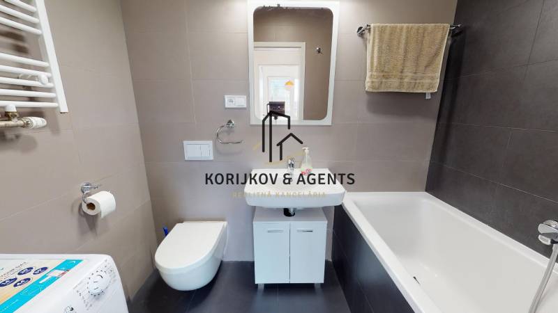 Koupelna s vanou, umyvadlem, závěsnou toaletou a pračkou v 2-pokojovém bytě.