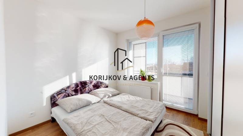 Světlá ložnice s velkou postelí, oknem a podlahou s dřevěným dekorem v 2-pokojovém bytě.