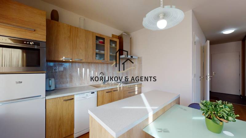 Kuchyně v 2-pokojovém bytě s dřevěným dekorem, vybavená spotřebiči a osvětlením.