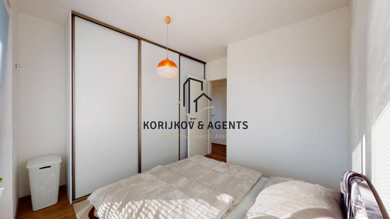 Ložnice v dvoupokojovém bytě s posuvnou skříní a postelí na podlaze s dřevěným dekorem.