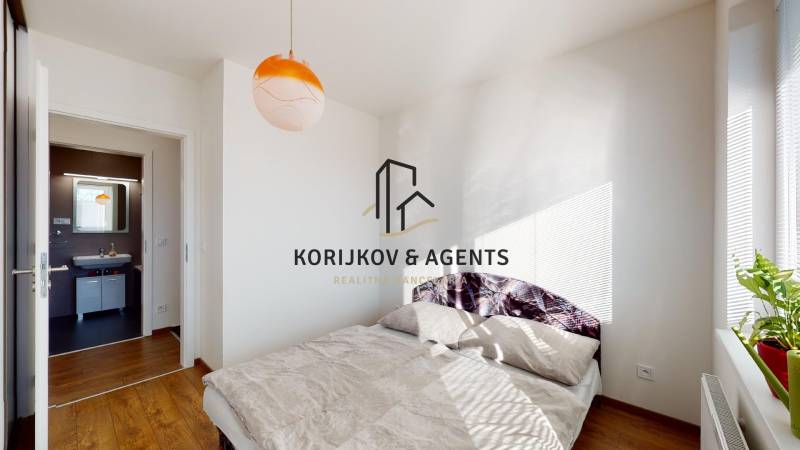 Ložnice dvoupokojového bytu s postelí a podlahou s dřevěným dekorem.