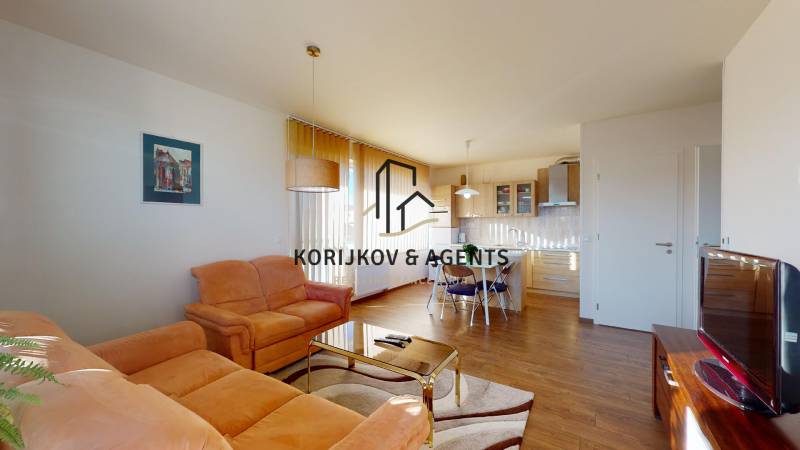 Obývací pokoj s oranžovou sedačkou, stolem a podlahou s dřevěným dekorem v dvoupokojovém bytě.