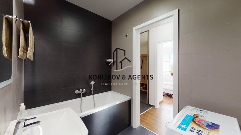 Koupelna v 2-pokojovém bytě s vanou a pračkou, podlaha s dřevěným dekorem.