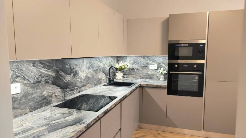 Kuchyně s tmavou pracovní deskou, vestavěnými spotřebiči a dekorativními květinami ve 4pokojovém bytě.