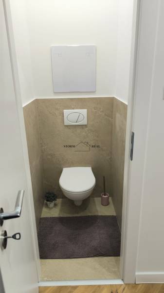 Toaleta s obkladem ve 4pokojovém bytě, podlaha s dřevěným dekorem, drobné dekorace.