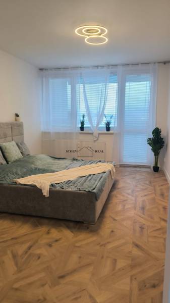 Světlá ložnice ve 4-pokojovém bytě s postelí čalouněnou látkou a podlahou s dřevěným dekorem.