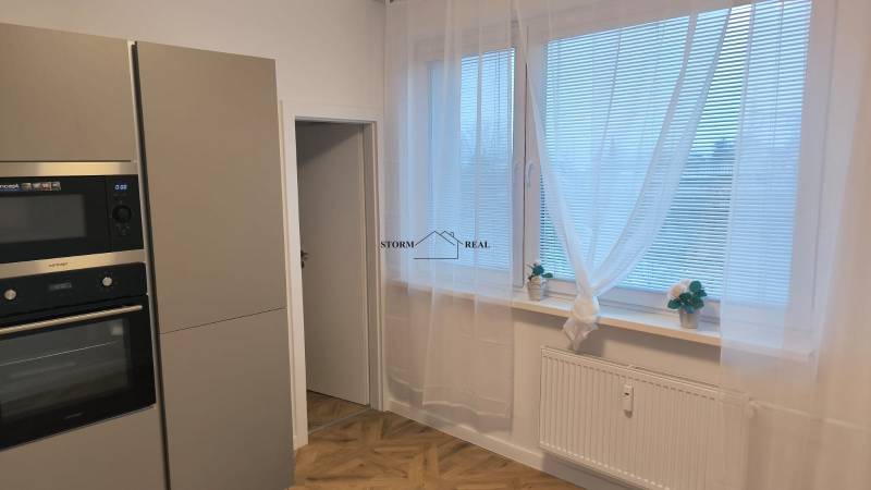 Interiér 4-pokojového bytu s podlahou s dřevěným dekorem, kuchyně s moderními spotřebiči.