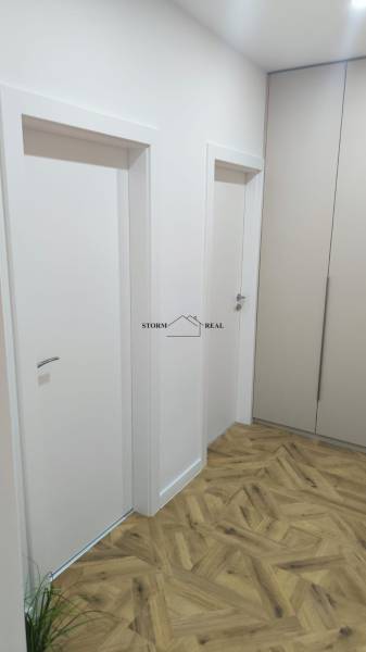 Interiér 4-pokojového bytu s bílými dveřmi, skříněmi a podlahou s dřevěným dekorem.