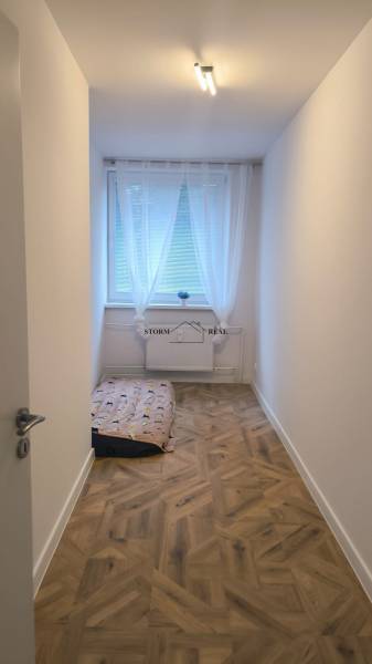 Úzký pokoj s velkým oknem a podlahou s dřevěným dekorem ve 4pokojovém bytě.