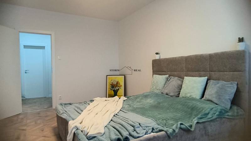 Ložnice ve 4pokojovém bytě s velkou postelí, podlahou s dřevěným dekorem a dekorací.