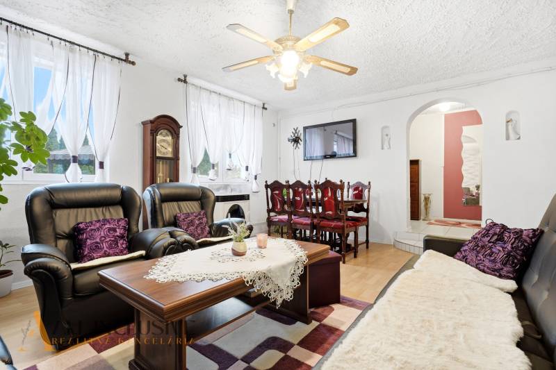 Obývací pokoj rodinného domu s krbem, černými sedačkami a podlahou s dřevěným dekorem.