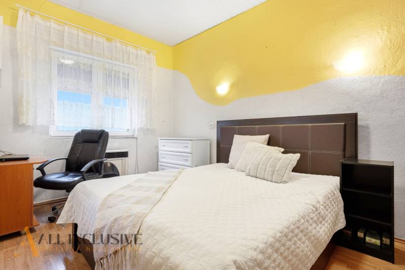 Ložnice v rodinném domě s postelí, křeslem a podlahou s dřevěným dekorem.