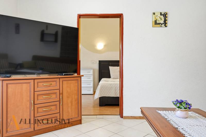 Interiér rodinného domu s velkou televizí, otevřené dveře do ložnice, dekorace.