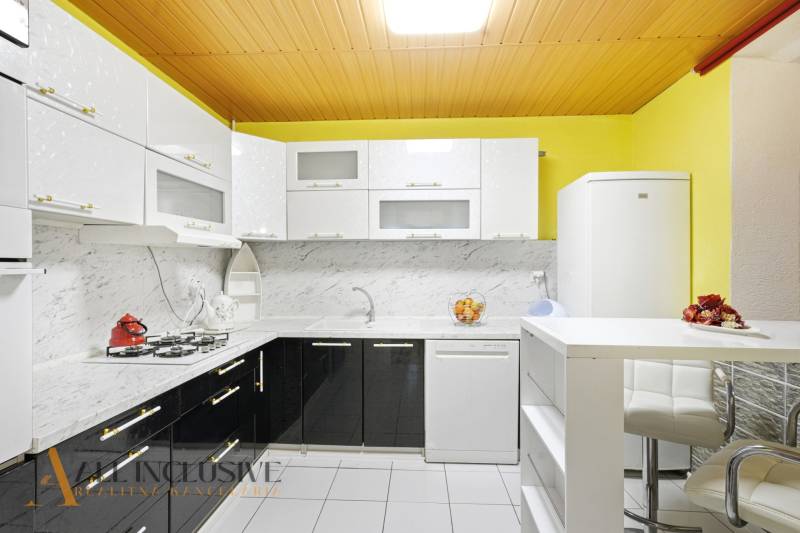 Kuchyně v rodinném domě se světlými skříňkami, mramorovým obkladem a bílými spotřebiči.