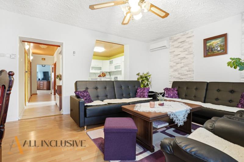 Obývací pokoj v rodinném domě s podlahou s dřevěným dekorem a černými koženými sedačkami.