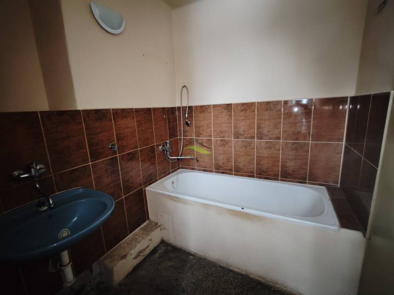 Koupelna s hnědými obklady, vanou a modrým umyvadlem v 2-pokojovém bytě.