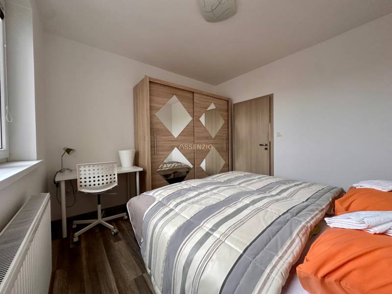 Ložnice v 3-pokojovém bytě s postelí, skříní, stolem a podlahou s dřevěným dekorem.