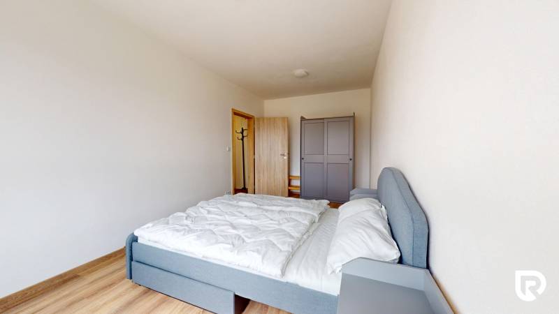 Ložnice ve 3-pokojovém bytě s postelí, šatní skříní a podlahou s dřevěným dekorem.