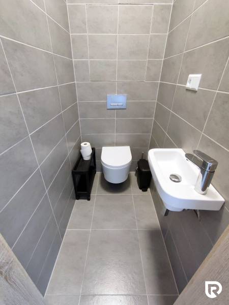 Koupelna s nástěnnou toaletou, umyvadlem a šedými obklady ve 3pokojovém bytě.