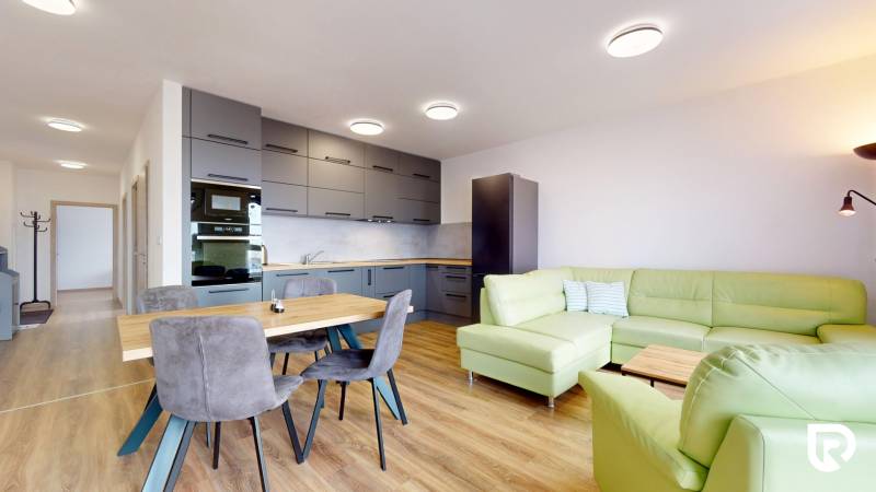 Kuchyně s obývacím pokojem ve 3-pokojovém bytě, zelená sedačka, podlaha s dřevěným dekorem.