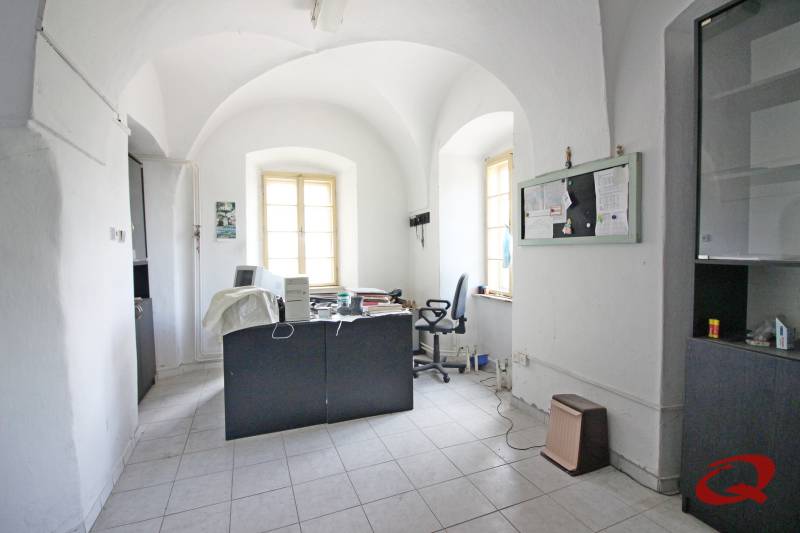 Kancelář v budově s oblými stropy, pracovní stůl a dvě okna.