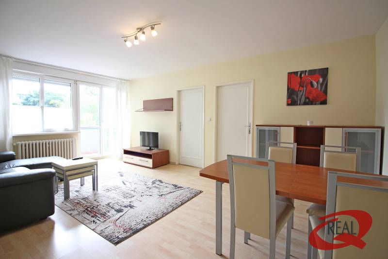 Obývací pokoj v 3-pokojovém bytě s podlahou s dřevěným dekorem, sedačkou a jídelním stolem.