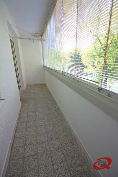 Zasklená lodžie s terakotovou dlažbou, stínidly a výhledem, vhodná pro 3-pokojový byt.