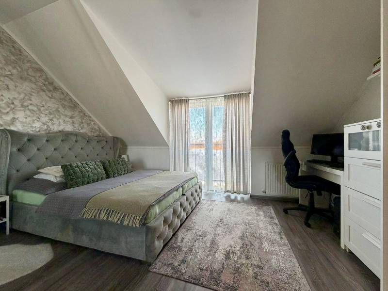 Ložnice v dvoupokojovém bytě s manželskou postelí, psacím stolem a podlahou s dřevěným dekorem.