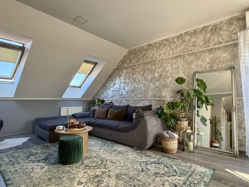 Obývací pokoj v 2pokojovém bytě s podlahou s dřevěným dekorem, rozkládací pohovkou a rostlinami.