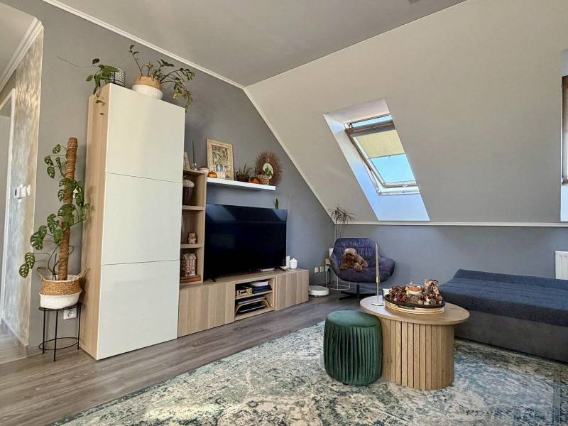 Obývací pokoj v dvoupokojovém bytě se střešním oknem, podlaha s dřevěným dekorem, pohodlný nábytek.