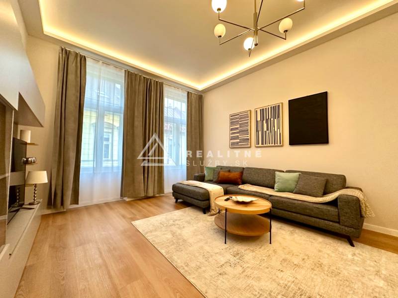 Obývací pokoj v 2-pokojovém bytě s podlahou s dřevěným dekorem, šedou sedačkou a dekorativními obrazy.