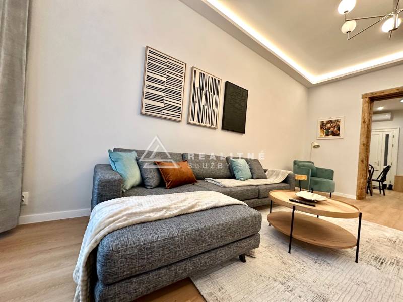 Obývací pokoj s pohovkou, podlahou s dřevěným dekorem a uměleckými díly ve 2pokojovém bytě.