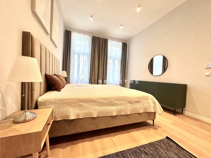 Ložnice v 2-pokojovém bytě s velkou postelí, lampou a podlahou s dřevěným dekorem.