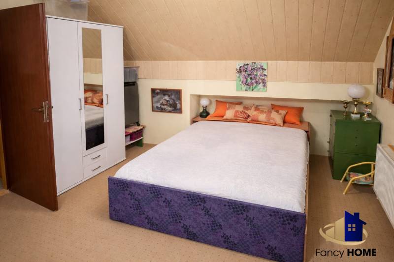 Ložnice v rodinném domě s postelí, bílou skříní a dekoracemi na stěně.