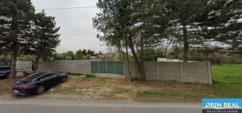 Pozemky - komerční na Dukelské v Bernolákově s betonovým plotem a příjezdovou cestou.