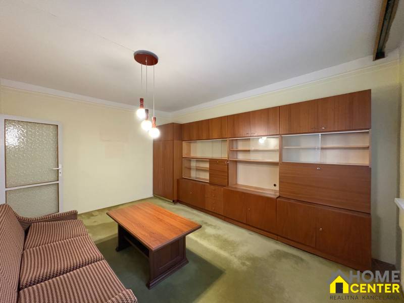 Obývací pokoj v 3-pokojovém bytě s dřevěnou stěnovou sestavou a gaučem.