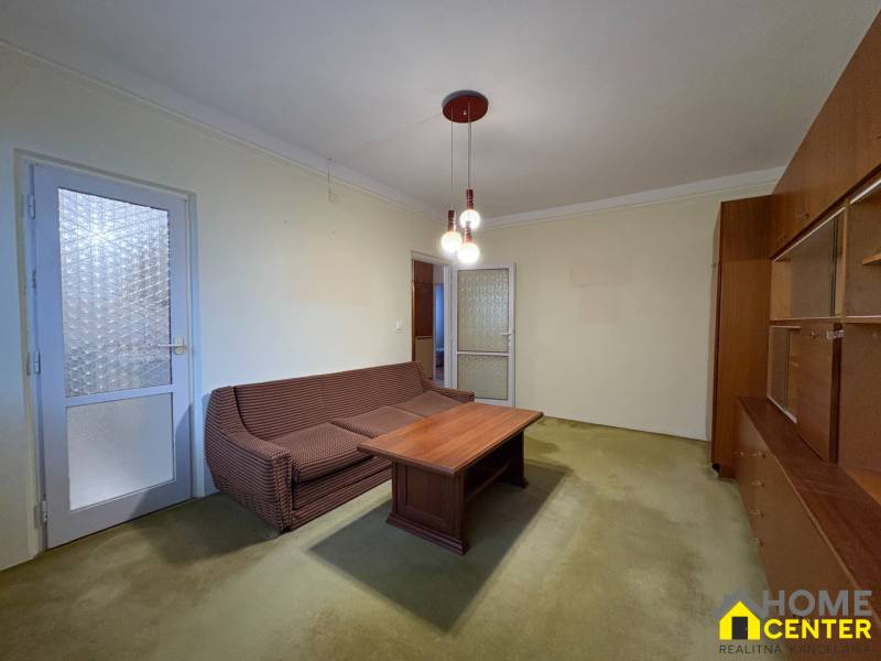 Obývací pokoj třípokojového bytu s pohovkou, konferenčním stolkem a vitrínou.