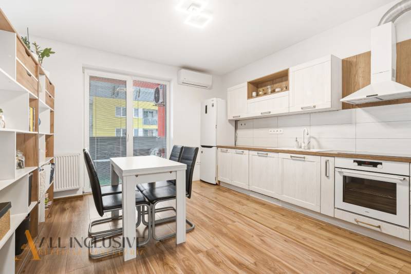 Kuchyně v 2pokojovém bytě s bílými skříněmi a podlahou s dřevěným dekorem.