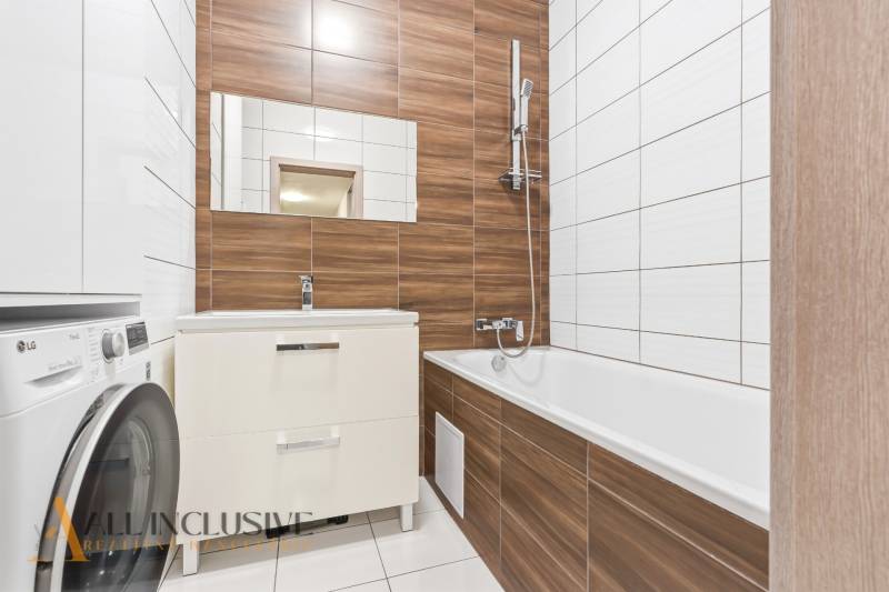 Koupelna v 2-pokojovém bytě s vanou, umyvadlem a pračkou. Využití dřevěného dekoru.