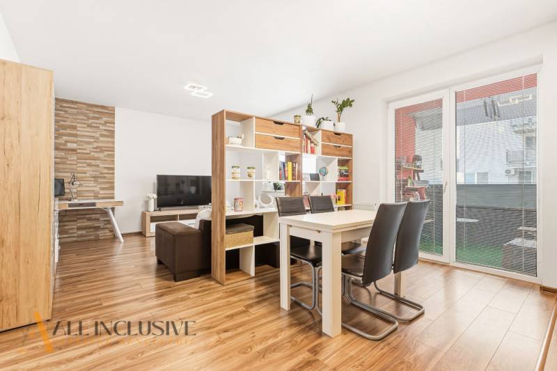 Obývací pokoj s jídelním stolem v 2-pokojovém bytě, podlaha s dřevěným dekorem, knihovna.