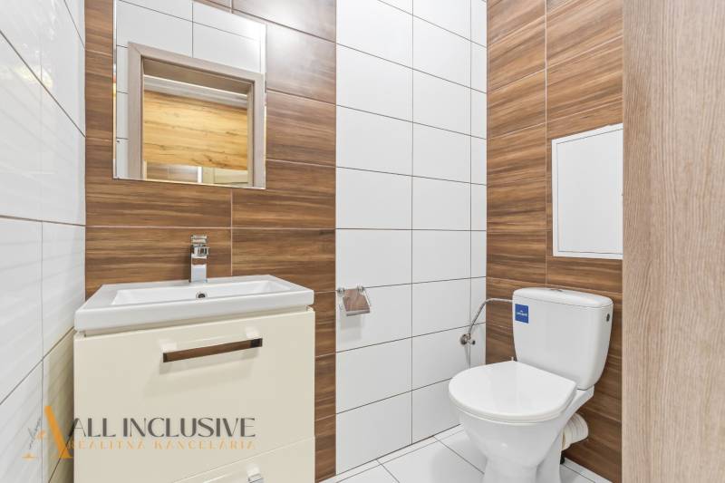 Koupelna v 2-pokojovém bytě s toaletou, umyvadlem a obklady s dřevěným dekorem.